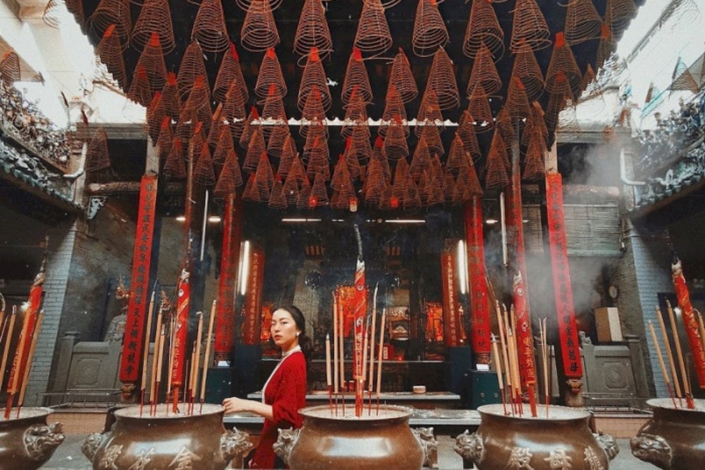 Young woman in a flowing red ao dai poses gracefully beside an ancient incense burner in the Temple's middle hall 
